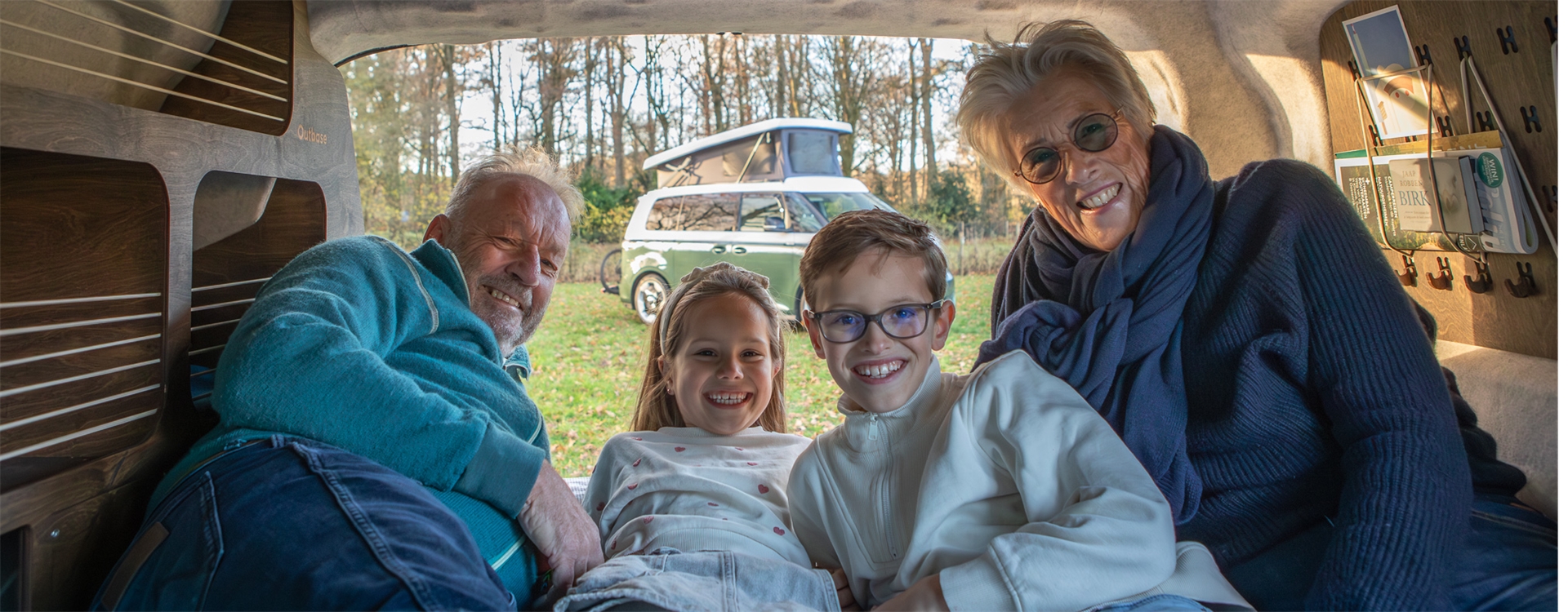 Twee volwassenen en twee kinderen liggen samen in een compacte camperbus met een ID.Buzz op de achtergrond