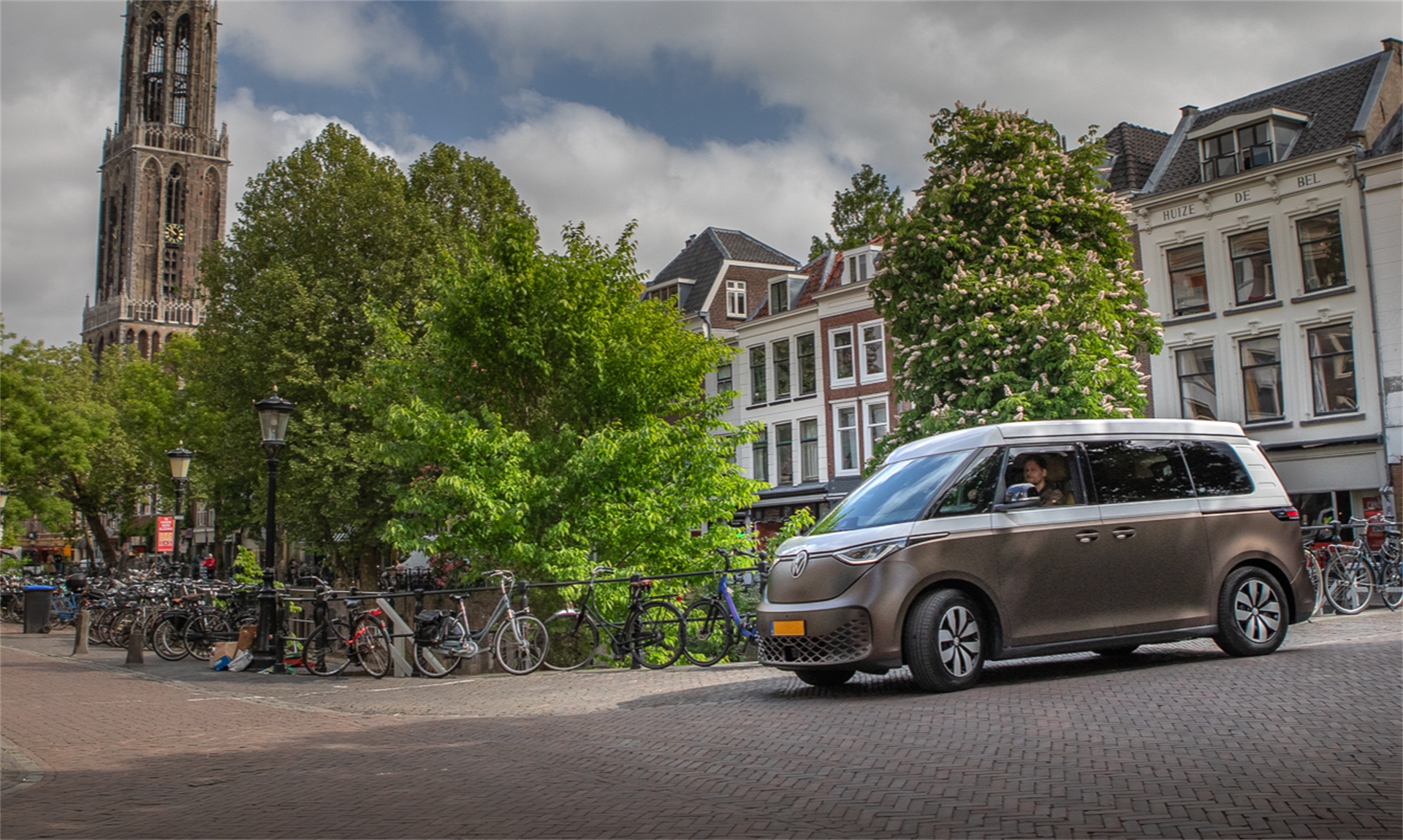 Elektrische compacte camperbus rijdt door het centrum van Utrecht, met zicht op de Domtoren Outbase Id.Buzz elektrische camper, voorziek van slimme keukenmodule en veel opbergruimte. 