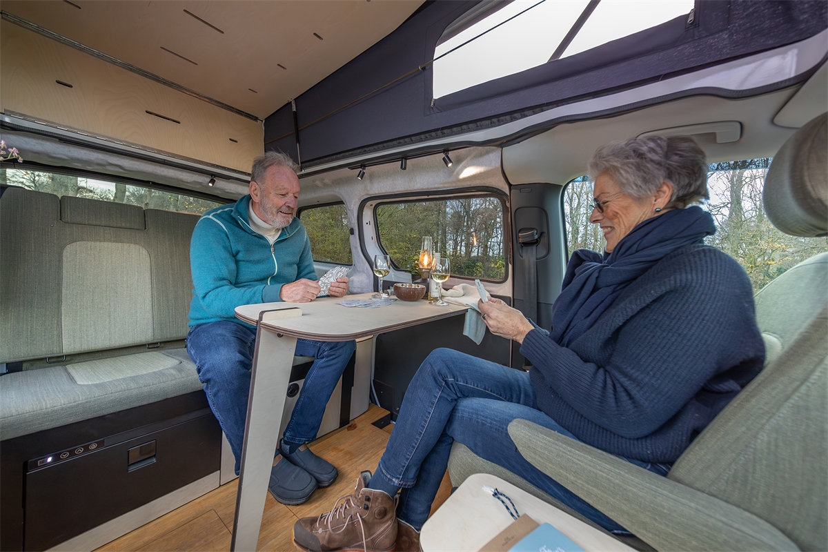 Twee mensen spelen een kaartspel aan de tafel in een compacte camperbus met slimme indeling