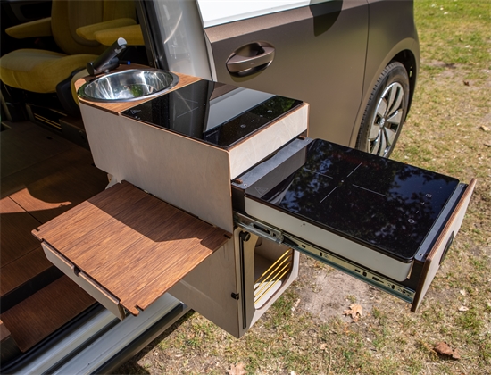 Slim uitklapbaar keukentje met spoelbak en inductiekookplaat aan een compacte elektrische camperbus